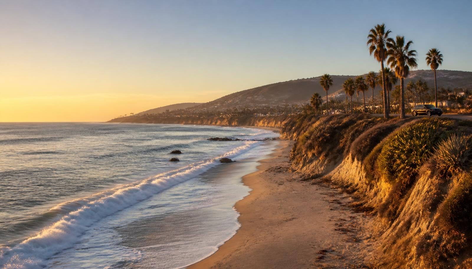 Southern California coastline at golden hour with Pacific Ocean waves, sandy beach, coastal bluffs and palm trees